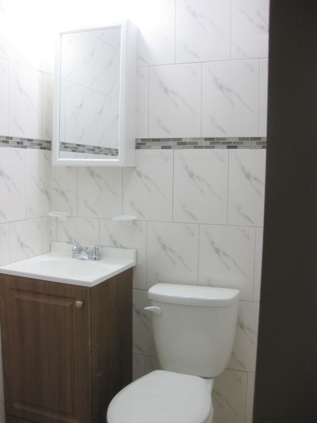 bathroom with vanity, toilet, and tile walls