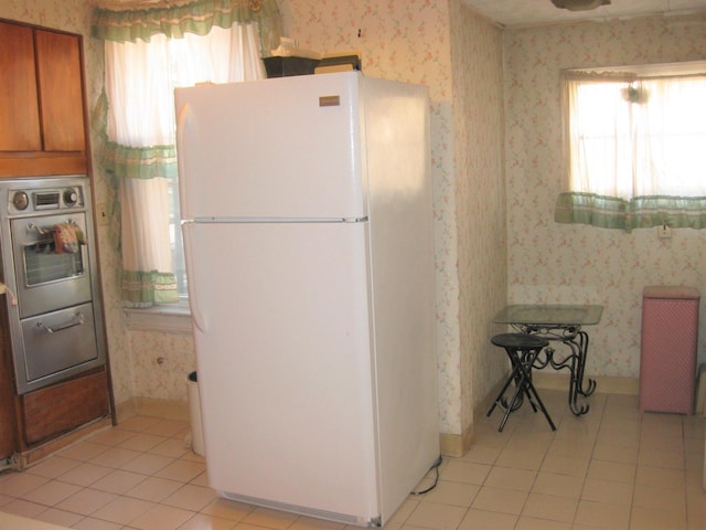 kitchen with oven, white refrigerator, light tile patterned floors, and a healthy amount of sunlight