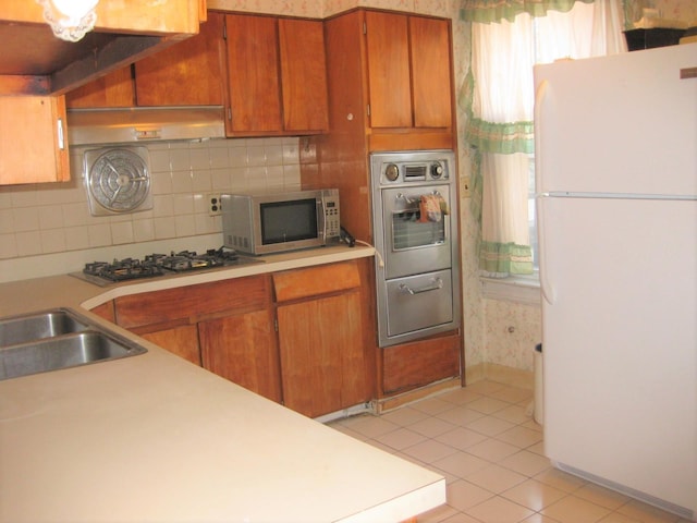 kitchen with sink, stainless steel appliances, backsplash, light tile patterned floors, and exhaust hood