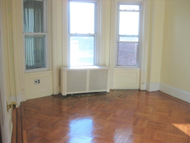 empty room with dark parquet flooring, radiator heating unit, and plenty of natural light