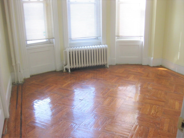 empty room with dark parquet floors, plenty of natural light, and radiator heating unit