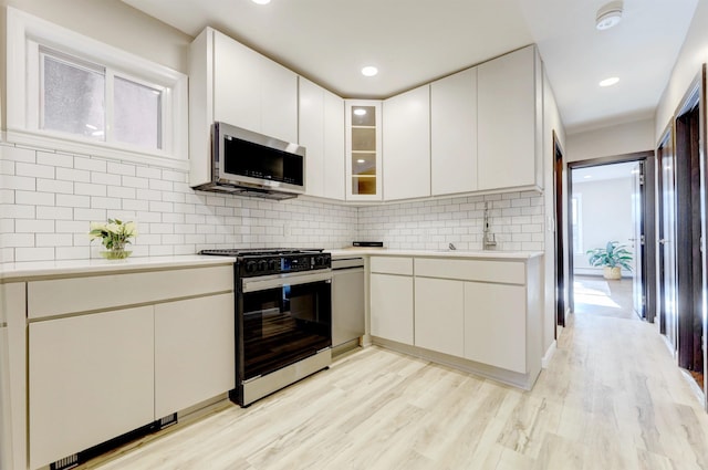 kitchen featuring sink, light hardwood / wood-style flooring, appliances with stainless steel finishes, decorative backsplash, and white cabinets