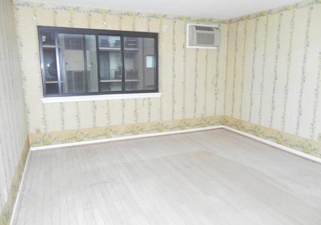 empty room featuring baseboards, a wall unit AC, wood finished floors, and wallpapered walls