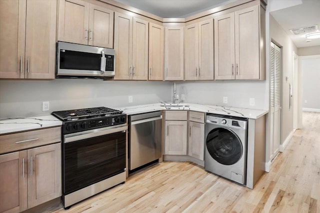 159 14th St Unit 4R, Hoboken, NJ 07030 - kitchen with washer / clothes dryer, appliances with stainless steel finishes, light wood-style flooring, and light stone counters