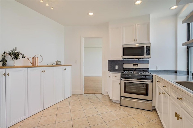 kitchen featuring decorative backsplash, appliances with stainless steel finishes, light tile patterned floors, and white cabinetry