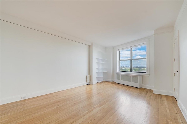 empty room featuring light wood-type flooring, radiator, and crown molding