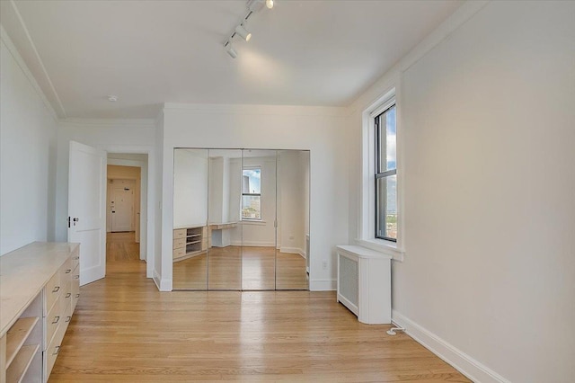 empty room with radiator heating unit, light hardwood / wood-style floors, track lighting, and ornamental molding