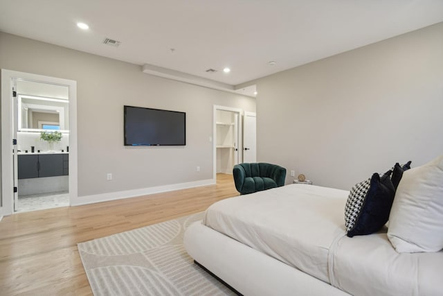 bedroom with a walk in closet, ensuite bathroom, and light hardwood / wood-style floors