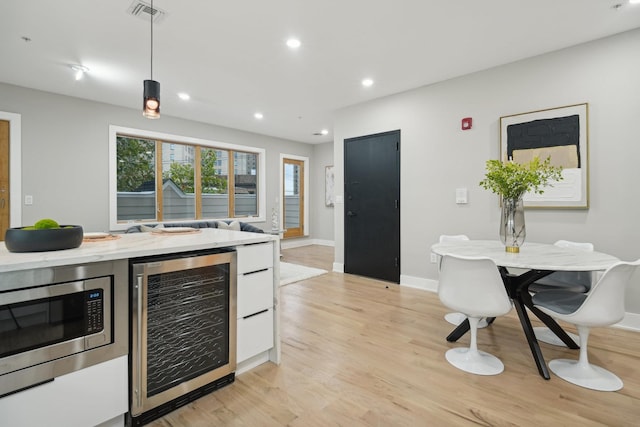 kitchen with light hardwood / wood-style flooring, hanging light fixtures, stainless steel microwave, light stone countertops, and beverage cooler