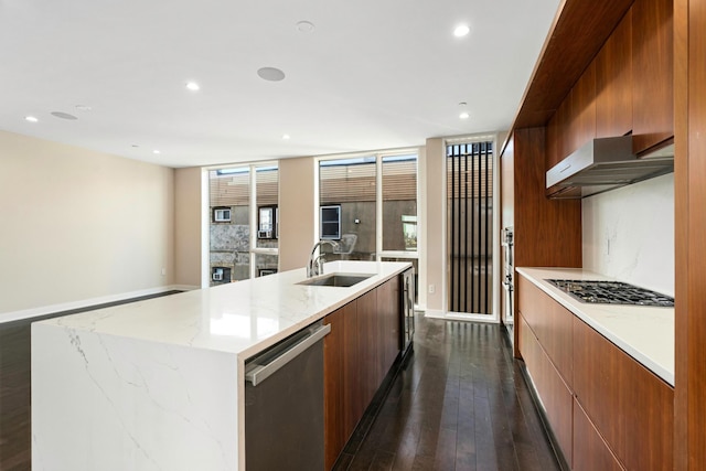 kitchen with modern cabinets, an island with sink, under cabinet range hood, a sink, and appliances with stainless steel finishes