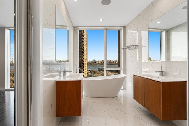 full bathroom featuring a water view, a freestanding bath, marble finish floor, and vanity