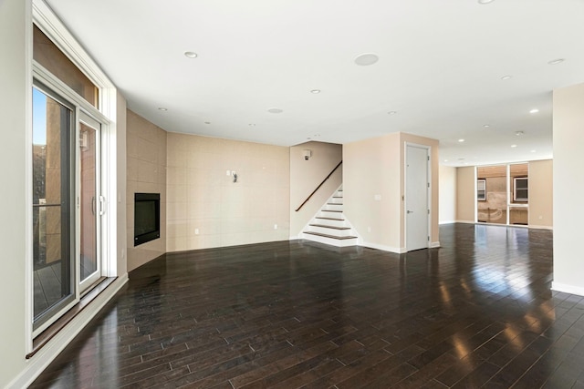 unfurnished living room with stairway, baseboards, hardwood / wood-style flooring, and a fireplace