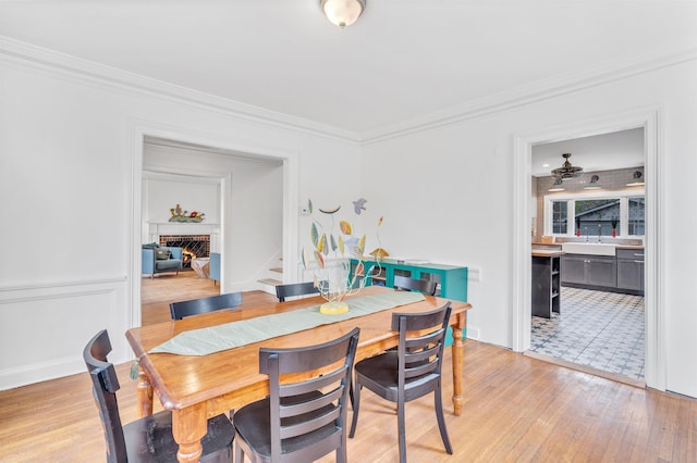 dining room with crown molding, stairs, a lit fireplace, and light wood-type flooring