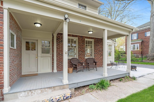 view of exterior entry with brick siding, fence, and covered porch