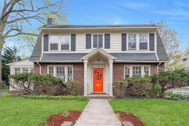 view of front of home with brick siding, a chimney, and a front lawn