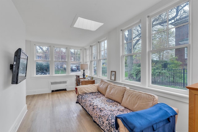 sunroom / solarium featuring baseboards, a skylight, radiator heating unit, and wood finished floors