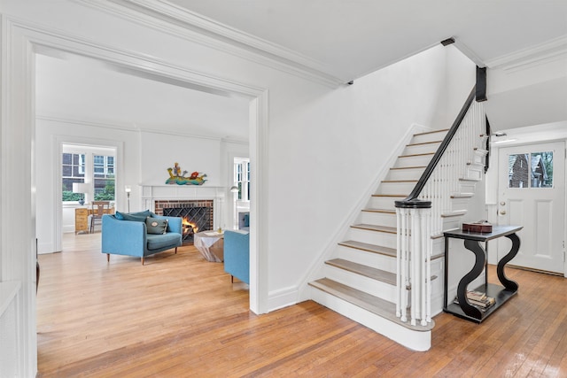 staircase with crown molding, a brick fireplace, and hardwood / wood-style floors