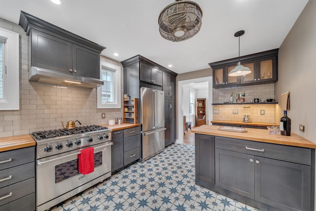 kitchen featuring wooden counters, light floors, tasteful backsplash, under cabinet range hood, and premium appliances