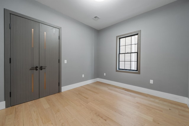 unfurnished bedroom featuring light wood-style floors, baseboards, visible vents, and a closet