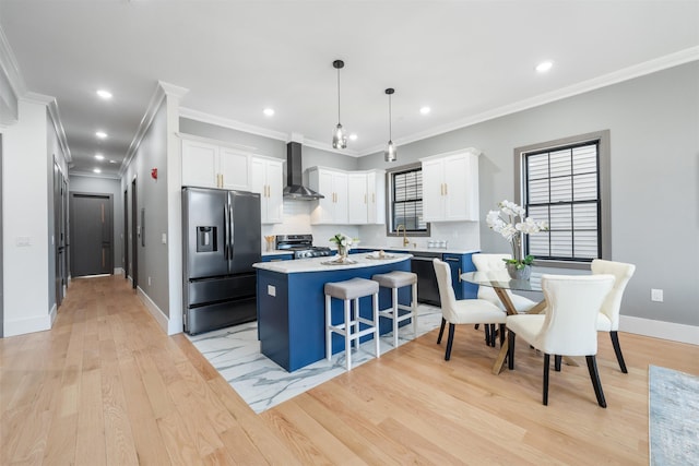 kitchen featuring wall chimney exhaust hood, appliances with stainless steel finishes, decorative light fixtures, a center island, and light countertops