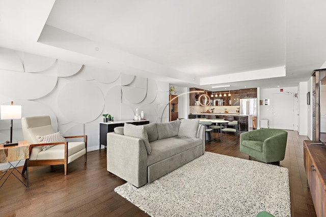 living area with a raised ceiling, baseboards, and dark wood-style flooring