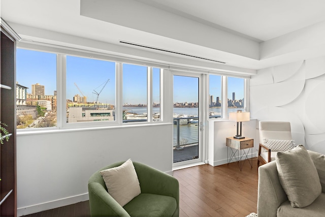 sitting room with baseboards, a view of city, a water view, and hardwood / wood-style flooring