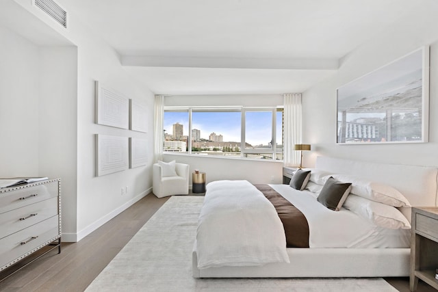 bedroom with visible vents, a view of city, baseboards, and wood finished floors