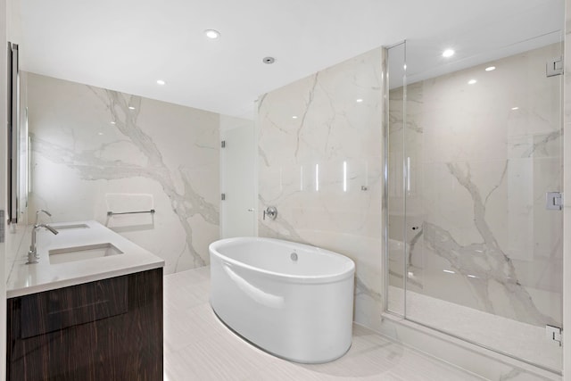 bathroom featuring a marble finish shower, a freestanding bath, tile walls, and a sink