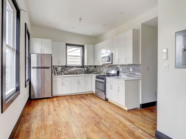 kitchen with tasteful backsplash, white cabinetry, appliances with stainless steel finishes, and light wood-type flooring