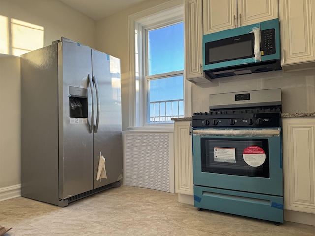 kitchen featuring stainless steel appliances, cream cabinetry, and stone countertops