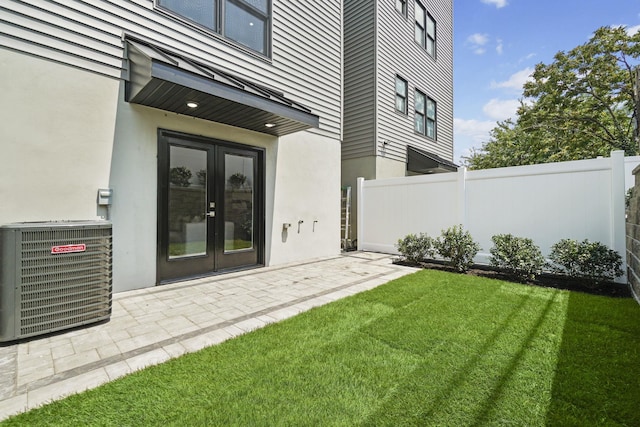 property entrance with central AC unit, a lawn, fence, french doors, and stucco siding