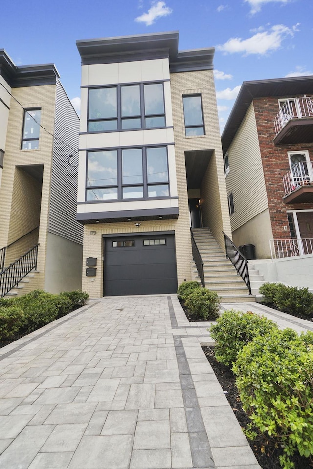 contemporary house with decorative driveway, brick siding, an attached garage, and stairs