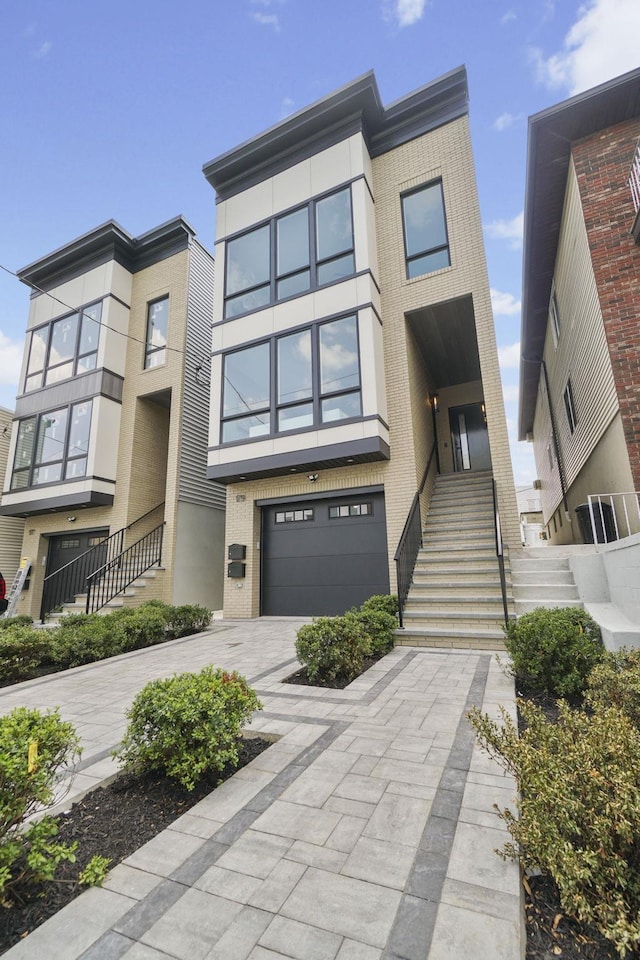 modern home featuring driveway, a garage, brick siding, stairway, and stucco siding