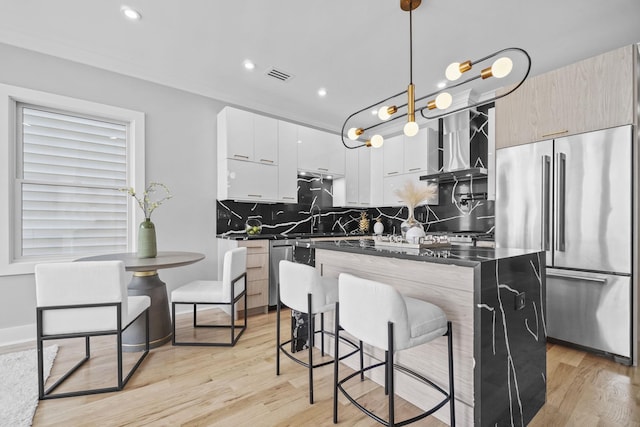 kitchen featuring visible vents, dark countertops, wall chimney exhaust hood, appliances with stainless steel finishes, and hanging light fixtures