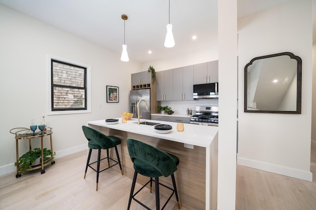 79 Vroom St Unit 1, Jersey City, NJ 07306 - kitchen with appliances with stainless steel finishes, light wood-style floors, a kitchen breakfast bar, gray cabinets, and a kitchen island with sink