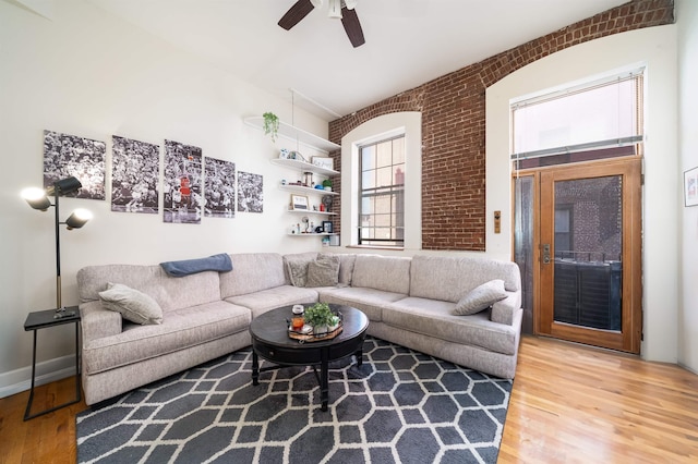 living room featuring ceiling fan, wood finished floors, and brick wall