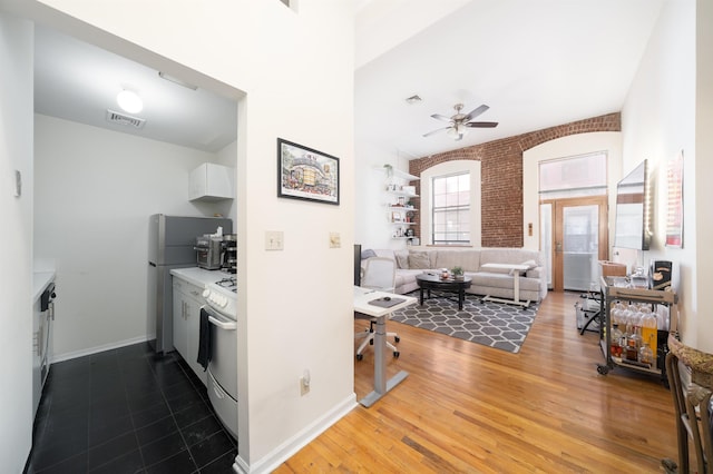 kitchen featuring wood finished floors, visible vents, brick wall, white range with gas cooktop, and white cabinets