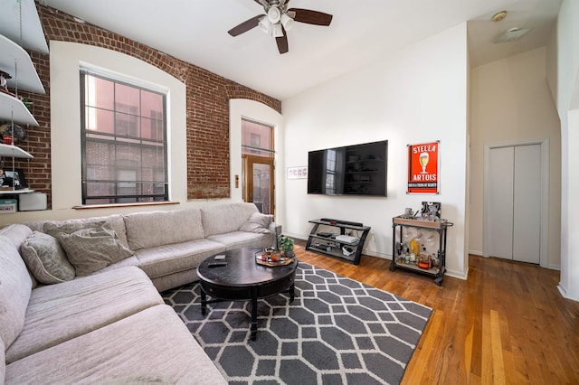 living area with wood finished floors, baseboards, brick wall, and ceiling fan