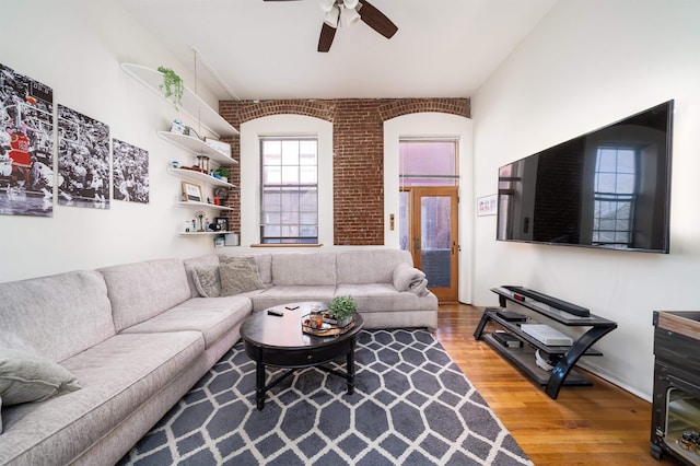 living room featuring a ceiling fan, light wood-style floors, and brick wall