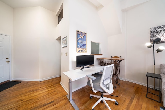 office space with baseboards, wood-type flooring, and high vaulted ceiling