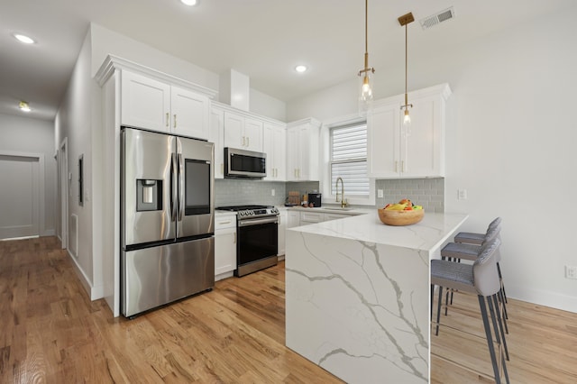 kitchen with light hardwood / wood-style floors, white cabinetry, kitchen peninsula, appliances with stainless steel finishes, and pendant lighting