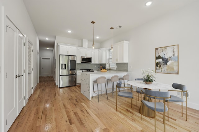 kitchen with stainless steel appliances, white cabinetry, kitchen peninsula, decorative light fixtures, and light wood-type flooring