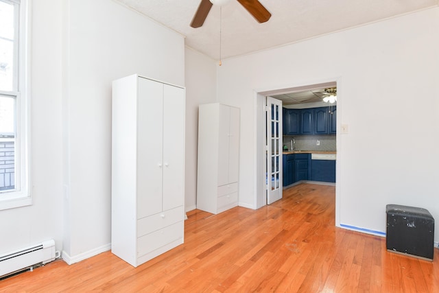 unfurnished bedroom featuring ceiling fan, a baseboard radiator, sink, and light hardwood / wood-style floors