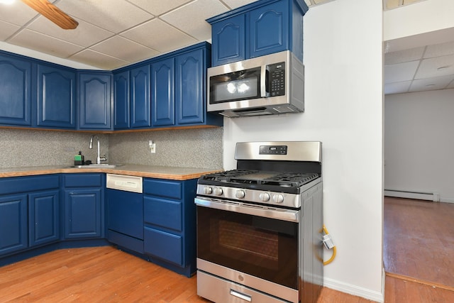 kitchen with sink, a paneled ceiling, appliances with stainless steel finishes, blue cabinets, and a baseboard radiator