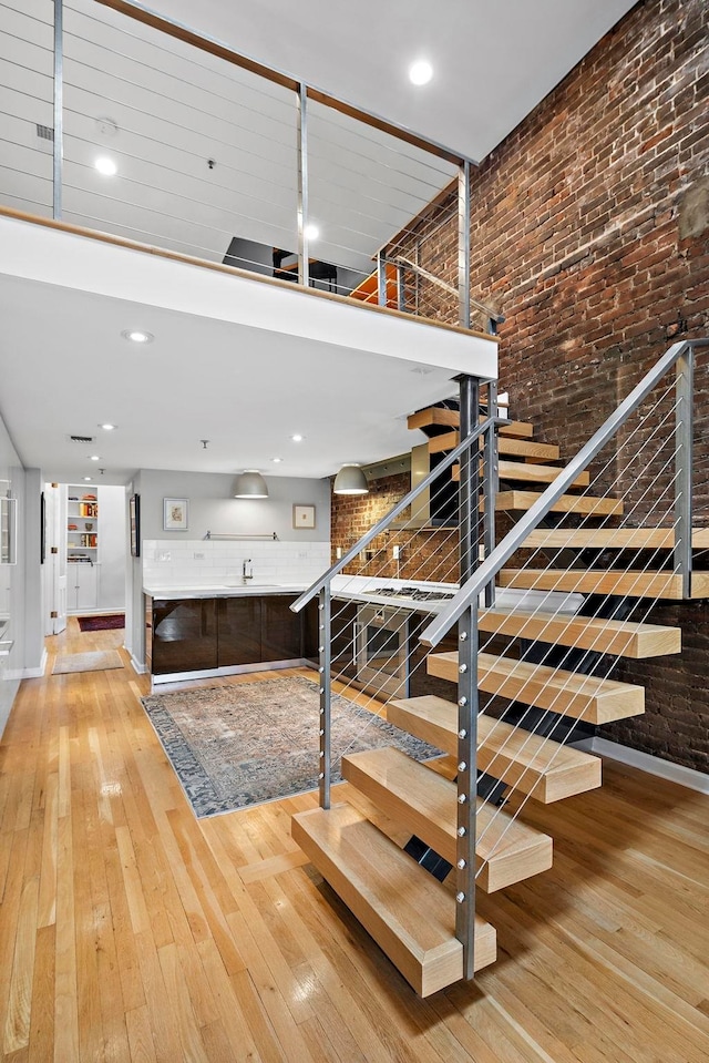 1110 Hudson St Unit 5B, Hoboken, NJ 07030 - stairway featuring hardwood / wood-style flooring, brick wall, baseboards, a towering ceiling, and recessed lighting
