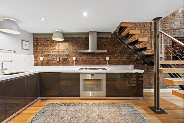 1110 Hudson St Unit 5B, Hoboken, NJ 07030 - kitchen featuring appliances with stainless steel finishes, wall chimney range hood, a sink, light wood-style flooring, and brick wall