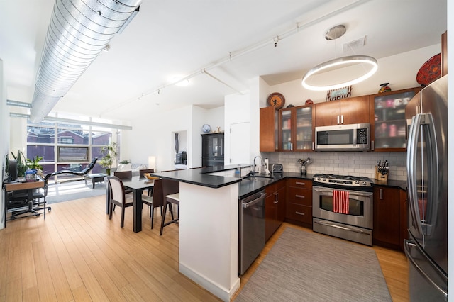 kitchen featuring a peninsula, a sink, appliances with stainless steel finishes, dark countertops, and tasteful backsplash