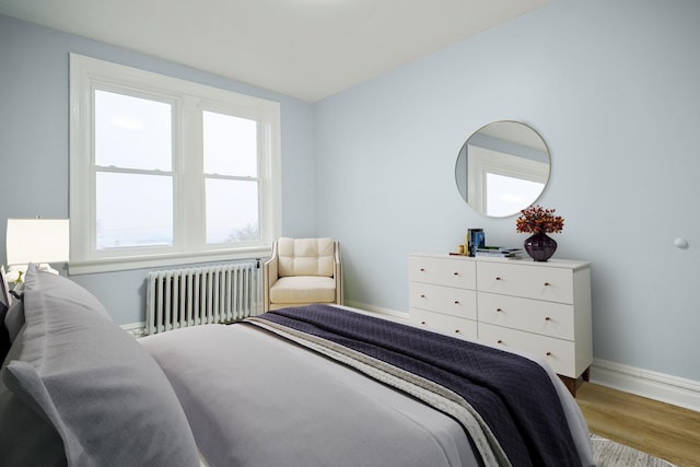 bedroom with radiator, wood finished floors, baseboards, and multiple windows