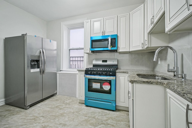 kitchen with appliances with stainless steel finishes, a sink, light stone counters, and white cabinets