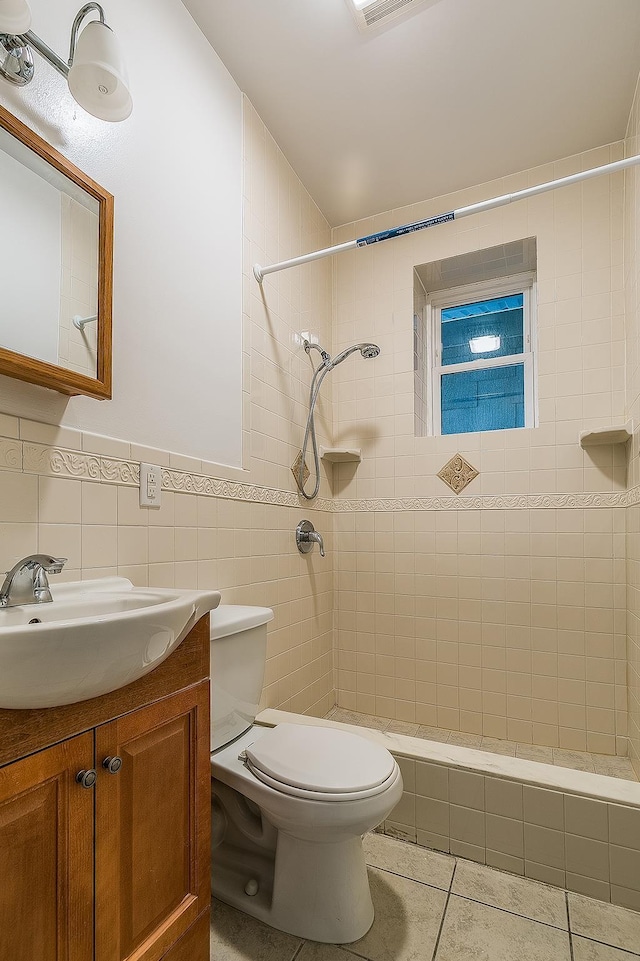 bathroom featuring tile patterned floors, toilet, tiled shower, vanity, and tile walls